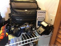 Overview of the two Olympus cameras, flashes, camera case, and strap all displayed on metal wire shelf