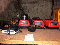 Three Black & Decker battery chargers with Firestorm battery pack, DeWalt charger and Lithium 20V charger all arranged on wooden surface.