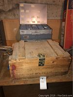 Photo showing large wooden boxes stacked with metal latch closures, worn and stained wood, some printed text on sides.