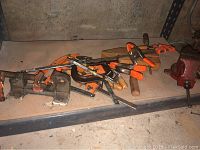 Various C clamps and a red Columbo metal vise on a wooden shelf.