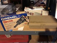 Photo showing two boxed tools and one beige case on a wooden shelf.