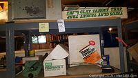 Shelf overview showing boxes of Lyman Turbo Tumbler, Trius Clay Target Trap, RCBS Piggyback II conversion unit, green metal loader, and cleaning solvent