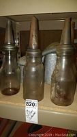 Three glass oil and gas containers with metal spouts on a shelf, showing aged translucent brown glass and threaded necks.