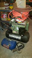 Front view showing Sears 20 gallon air compressor with hoses coiled on top, white bucket, and smaller blue Mobile Air compressor unit