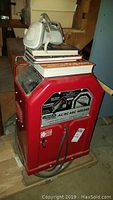 Overview of red Lincoln Electric AC/DC arc welder with welding books and respirator mask on top