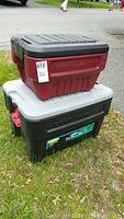Two ActionPacker utility boxes stacked outdoors, one smaller red with black lid on top of larger black with gray lid box.