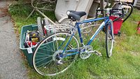 Blue Shogun Cr Mo 300 bicycle with Bell branded black seat, foam handle grips, visible rust on frame and metal parts outdoors on grass and concrete.