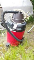 Full view of red and black Shop Vac 16-gallon wet/dry vacuum with hose, power cord coiled on top, placed on grass outdoors.
