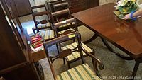 Six mahogany dining chairs around a table, five straight backs and one captain's chair, upholstered striped seats visible.