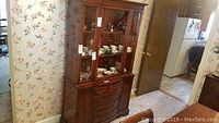 Front view of the mahogany china cabinet showing glass display doors, drawer below, and lower cabinet doors with hardware. The cabinet holds various china items inside visible through the glass.