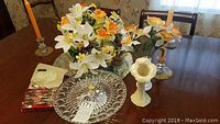 Photo showing artificial flowers in Belleek porcelain vases, crystal plate, collectible spoons in pouch, and candle holders on a wooden table.