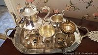 Silver plated tea set including teapot, sugar dish, creamer, salt and pepper shakers, waste bowl, all on a large serving tray with ornate handles.