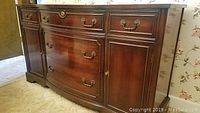 Front view of mahogany buffet showing three small drawers at top, two large drawers in center, and two cabinets on sides with ornate brass handles.