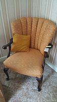 Front view of the vintage Queen Anne style chair showing curved fan-back, light tangerine fabric upholstery, carved dark wooden arms and legs, with small mustard yellow pillow on seat.