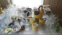 Overview of assorted glassware including lemon-shaped pitcher and mugs, Wedgwood plate, Christmas mugs, apothecary bottles, and novelty ceramics.