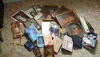 Wide view of lot showing framed religious prints, books, rosaries, and crucifix statue on carpeted floor