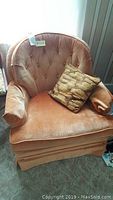 Tangerine velveteen tufted back Jessup armchair with a patterned pillow on the seat, showing wear on the fabric.