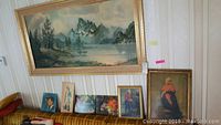 Framed and unframed vintage style prints shown on wall and couch, including large mountain lake landscape print and smaller portraits