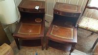 Two matching mahogany end tables side by side showing tiered structure and surface wear.