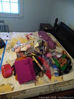 Overview of bed with various scarves, yarn bundles, gloves, and folded sweaters including white hand knit sweater