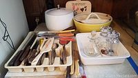 Wide view of vintage white ice bucket, yellow Pyrex casserole dish, white ceramic serving dish with blue floral pattern, cutlery organizer with assorted vintage silverware, glass cruet set, and salt and pepper shakers on white ceramic tray.