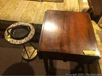 Photo showing the wooden drop leaf end table and the standing ashtray side by side on a carpeted floor in front of a couch.