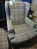 Wingback chair with cushioned seat and plaid fabric upholstery, showing armrest and winged back.