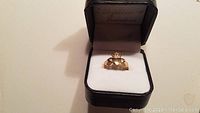 Front view of the gold Claddagh ring inside black protective jewelry box with white padding.