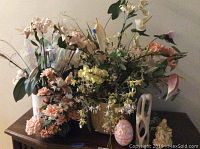 Overall view of three faux flower decor pieces, egg trinket box, stone sculpture, and religious decor items arranged on table