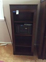 Full view of the tall narrow wooden bookcase showing three shelves and decorative molding on top and bottom.