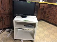 Vizio 22 inch flat panel TV on top of white laminate two shelf rolling cart, visible remote in the middle shelf, kitchen background