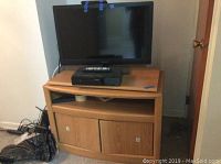 Full view of flat panel TV on top of wood rolling media cart with storage below.