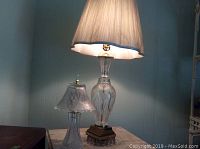 Two glass and brass-tone table lamps on a marble table; one smaller all-glass lamp and one taller lamp with brass base and scalloped shade.