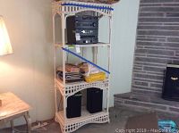 Photo showing the full height and width of the three-shelf white rattan shelving unit with various items on shelves (not included).