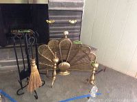 Wrought iron tool stand with four tools alongside brass scalloped shell fireplace cover and brass andirons in front of fireplace