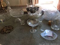 Wide shot showing multiple crystal and cut glass serving pieces on carpet, including footed bowls, ice bucket, and brass anchor trivet.