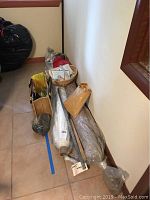 Various fabric rolls and sewing tools stacked against a wall with some baskets and bags included.