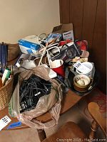 Table with Panasonic phones, black cords in plastic bag, pens, surge protectors, and other miscellaneous office supplies and accessories piled on it.