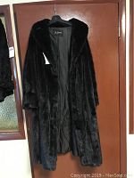 Full view of the full-length dark mink fur coat hanging on a door.