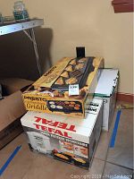 Stacked boxed appliances showing Presto Cool Touch Electric Griddle on top and Tefal Safety Super Fryer box below.