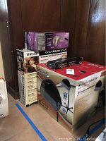 Photo showing boxed Modern Elements Ion Pro hair dryer, Homedics BackExpert 2000 back massager system, and other boxed health and styling items stacked on floor.