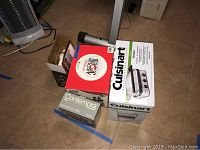 Photo showing boxed Cuisinart Griddler, Contempra indoor grill box, KitchenAid hand mixer and Magic Bullet accessories stacked together on floor