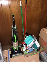 Full view of Bissell vacuum and box with cleaning supplies including brooms, dustpans, brushes, and spray bottles