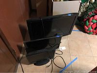 Three flat screen TVs stacked against a wall, the largest is Panasonic 32 inch, others smaller sizes are visible
