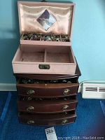 Pink vintage jewelry box with satin interior and compartments for earrings visible on wooden dresser.