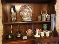 Shelf with two pairs of brass candle holders, Capodimonte rose candle holders, Asian inspired vase, decorative plates, and Japan China tea set.