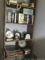 Shelves showing eight clocks of different styles, vinyl records, VHS tapes, DVDs, and decorative items.