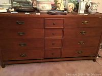 Front view of 9 drawer wooden dresser with brass handles, showing wooden construction and condition including some scratches on legs