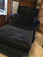 Blue faux velvet armchair with attached lumbar pillow and matching ottoman placed in a room, showing front view of the chair and top view of ottoman.