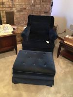 Armchair and ottoman upholstered in blue faux velvet placed on carpeted floor in living room setting.